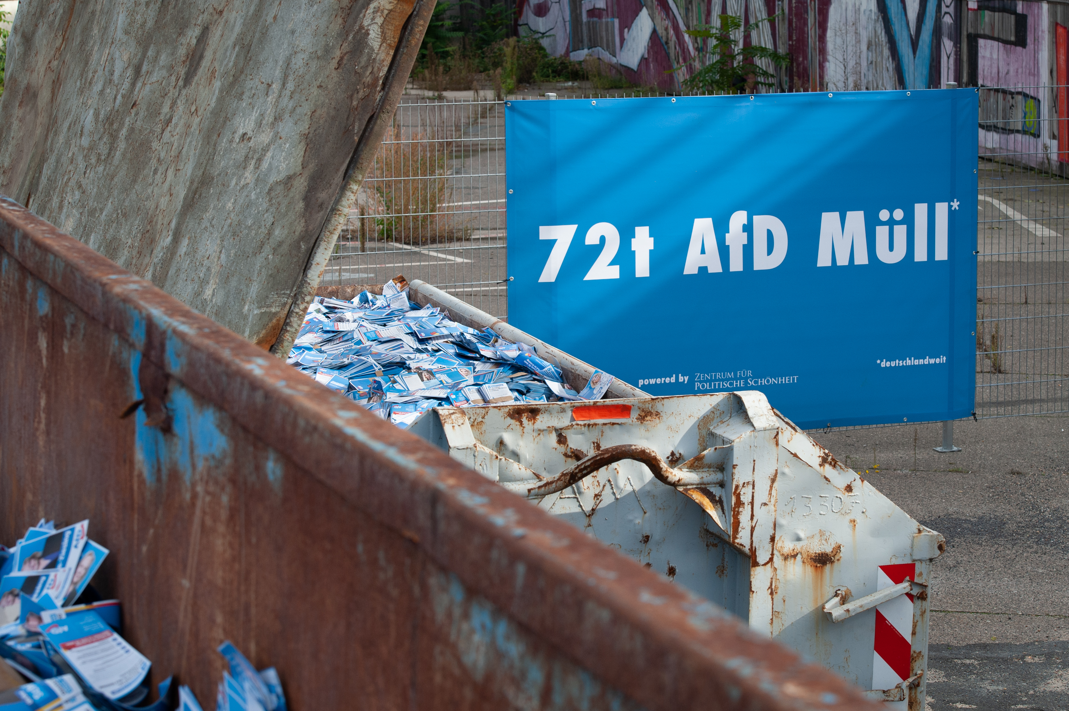 Two containers with AfD campaign flyers seen in birds perspective. In the backrgound a banner stating “72t AfD Müll powered by Zentrum für Politische Schönheit”, meaning “72 tons of AfD-trash“.